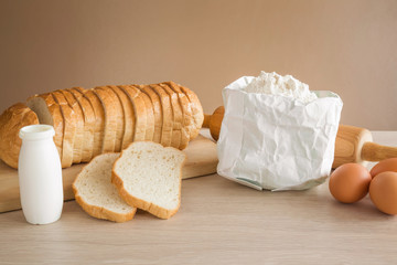 Fresh sliced bread on the wooden board with flour, milk and eggs in the kitchen. Healthy eating and lifestyle.