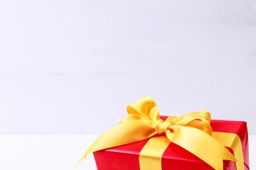 Gift box with yellow bow. Present wrapped with ribbon. Christmas or birthday red package. On white wooden table.
