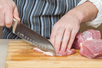 Chef's hands with a knife cuts the meat on the wooden board in the kitchen. Cooking at restaurant. Healthy eating and lifestyle.