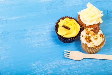 Cupcakes with buttercream. Sweet cake with cream and small chocolate bar. Dessert with topping and fork. On blue wooden rustic background.