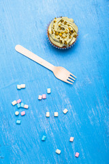 Cupcake with buttercream. Sweet cake with pistachio cream. Dessert with topping and marshmallows. On blue wooden rustic background.