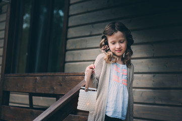 child girl with candle holder relaxing in evening at cozy country house. Kid spending summer vacation in log cabin in the woods