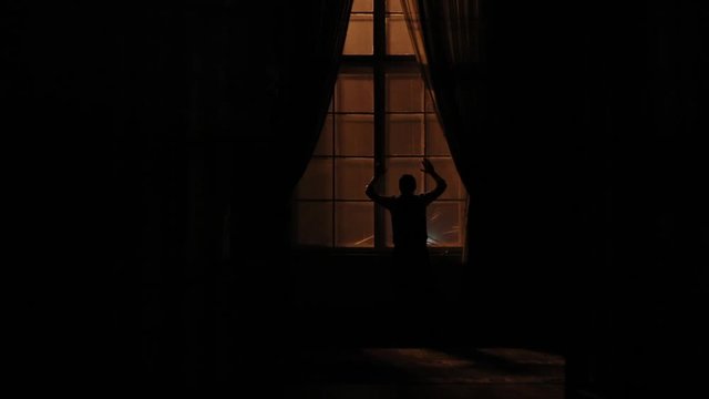 The back view of the depressed man hitting the window in the dark room.