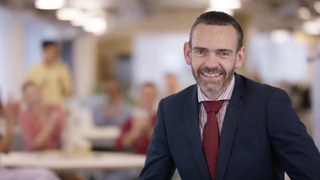  Portrait smiling business manager in office with staff clapping in background