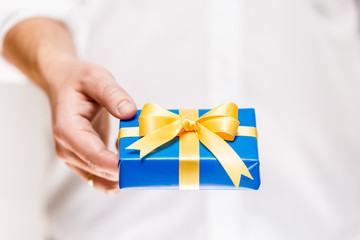 Male hand holding a gift box. Present wrapped with ribbon and bow. Christmas or birthday blue package. Man in white shirt.