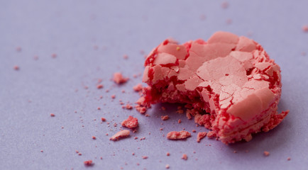 Pink bitten macaroon with crumbs on purple background