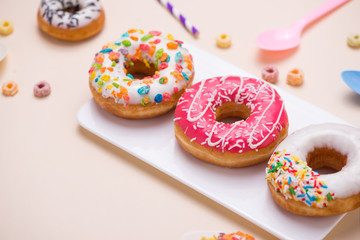 Party. Different colourful sugary round glazed donuts and bottles of drinks on light color background.
