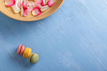 Macaroon cakes. Different types of macaron. Colorful almond cookies. Rose petals in bowl. On blue wooden rustic background.