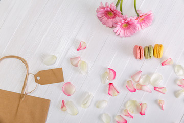 Macaroon cakes with shopping bag and Gerbera flowers. Different types of macaron. Colorful almond cookies. On white wooden rustic background.