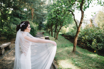 Bride whirls her veil walking along the path in park