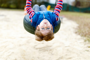 Funny kid boy having fun with chain swing on outdoor playground