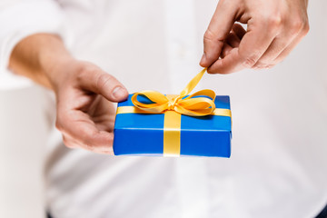 Male hands holding a gift box. Present wrapped with ribbon and bow. Christmas or birthday blue package. Man in white shirt pulls the ribbon.