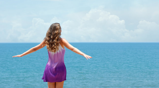Carefree happy woman in dress and free open arms on coast at sunny day.