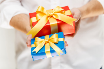 Male hands holding a gift boxes. Present wrapped with ribbon and bow. Christmas or birthday red, blue package. Man in white shirt.