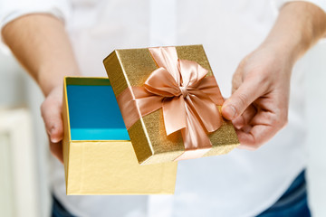 Male hands holding a gift box. Opened present wrapped with ribbon and bow. Christmas or birthday golden paper package. Man in white shirt.