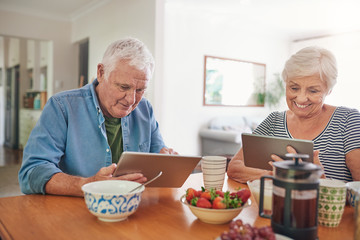 Smiling seniors using digital tablets over breakfast at home