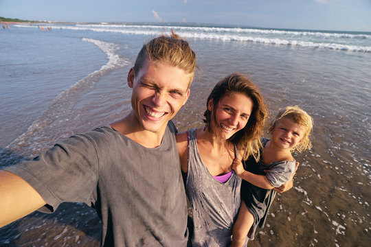 Vacation and technology. Happy family with kid taking selfie together on smartphone on beach.