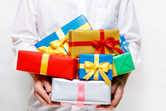 Male hands holding a gift boxes. Presents wrapped with ribbon and bow. Christmas or birthday colored packages. Man in white shirt.