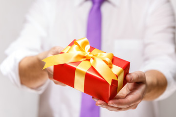 Male hands holding a gift box. Present wrapped with ribbon and bow. Christmas or birthday red package. Man in white shirt and necktie.