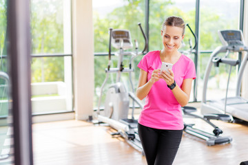 Fototapeta premium Sport lifestyle and technology. Attractive young woman using smartphone in gym.