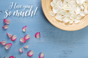 Petals of white and pink roses on blue painted rustic background. I love you so much. Dirty grunge wooden board.