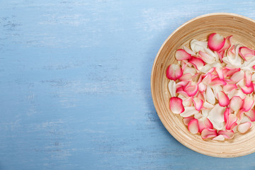 Petals of white and pink roses on blue painted rustic background. Fresh natural flowers in bowl. Dirty grunge wooden board.