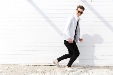 Cheerful man in sunglasses running over white wall background