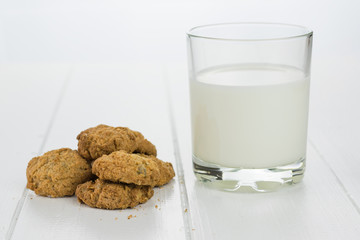 A glass of milk and homemade cookies on white wooden table.