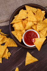 Nachos chips. Delicious salty tortilla with sweet salsa or chilli sauce on wooden background. Snack on rustic plate.