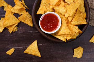 Nachos chips. Delicious salty tortilla with sweet salsa or chilli sauce. Snack on rustic plate. Sackcloth on wooden background.