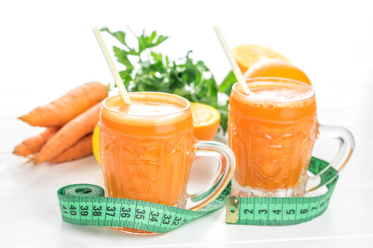Measuring tape, carrot smoothie with orange on white wooden table.