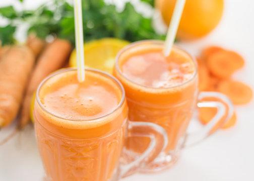 Two glass mugs with carrot smoothies and greens on a white wooden table.