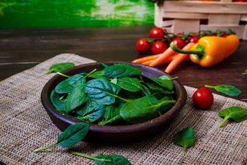 Spinach leaves in bowl. Carrot, pepper and cherry tomatoes. Raw fresh vegetable. Fresh natural plant leaf. Organic food on wooden table.