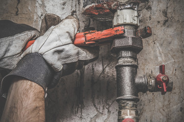 Man's hand in protective glove working with wrench at pipe. Plumbing. Vintage style.