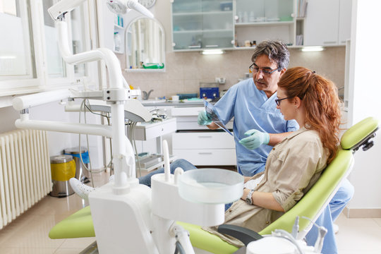 A professional dentist, equipped with a bright smile, converses with his red-haired female patient, carefully explaining the upcoming treatment, and ensuring her comfort throughout the process.