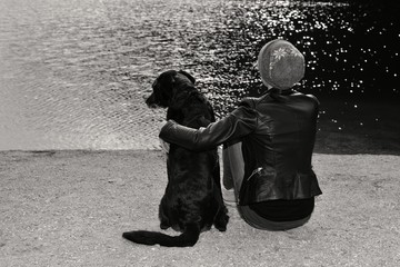 Junge Frau sitzt mit ihrem Labradormischling an einem Seeufer