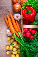 Vegetables. Potatoes, carrot and red pepper. Lettuce salad, garlic and brocoli. Onion and radish. Wooden basket on rustic table.