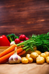Vegetables. Potatoes, carrot and red pepper. Garlic and brocoli. Onion and radish. Wooden basket on rustic table.