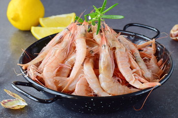 Raw fresh shrimps in a black metal bowl with rosemary on a grey background. Mediterannean lifestyle. Healthy food.