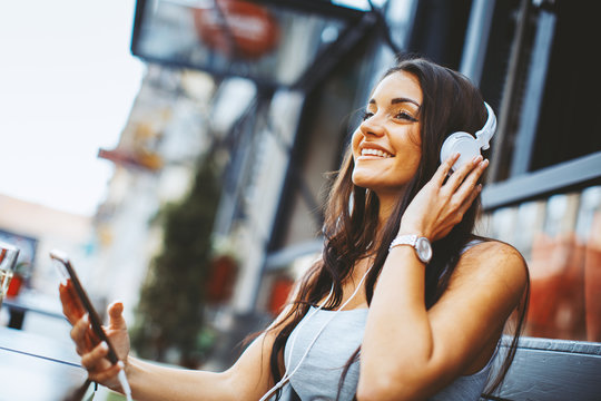 Beautiful young woman listening to music in sidewalk cafe via headphones