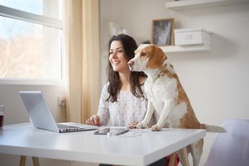 Businesswoman looking through window with her dog in home office . Businesswoman in thirties concept