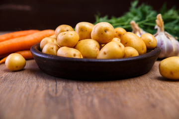 Potatoes in plate. Carrot, garlic and raw new potato. Fresh natural vegetables. Organic bio food on rustic wooden table.