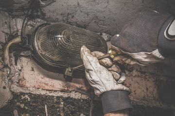 Man's hand in protective glove working with screwdriver. Electrician changing lamp bulb. Dangerous job. Vintage style.