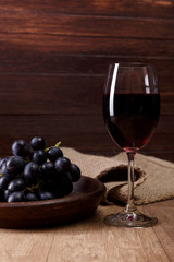 Red wine. Wineglass with dark grapes branch on plate. On rustic wooden background.