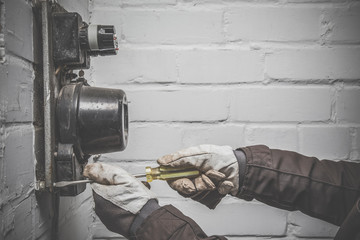 Man's hand in protective glove working with screwdriver. Electrician repair old electric meter....