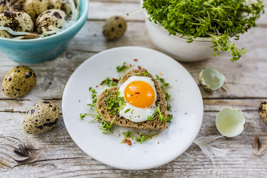 Roasted quail egg with cress on the bread on a wooden background.