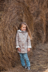 Naklejka na ściany i meble Portrait of a small beautiful girl near the haystacks