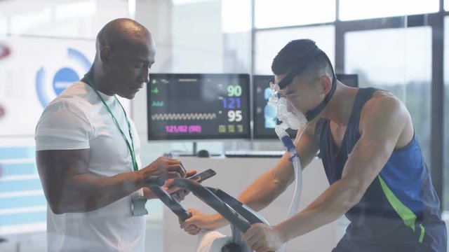  Sports professional analyzing man's fitness levels with hi tech equipment. Professional athlete in training, personal trainer at the gym or scientific research concept. 
