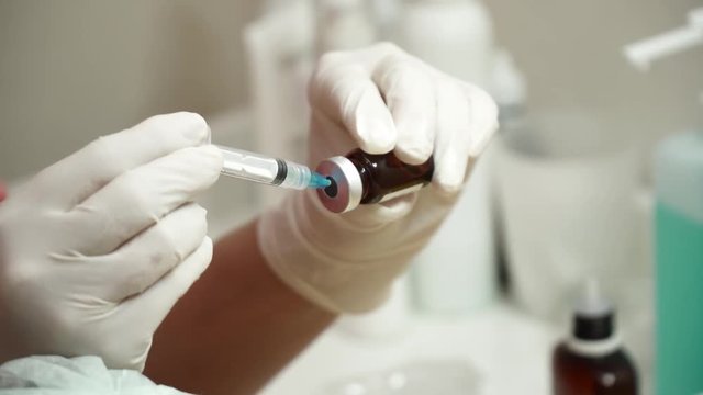 Beautician filling in the medical syringe with anti aging liquid closeup