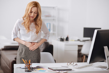 Miserly young businesswoman feeling stomachache in the office